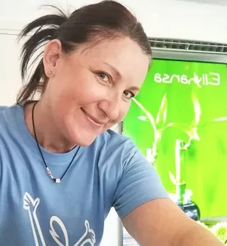 Smilende ansatt i blå t-skjorte foran grønn Ellyhansa-plakat.